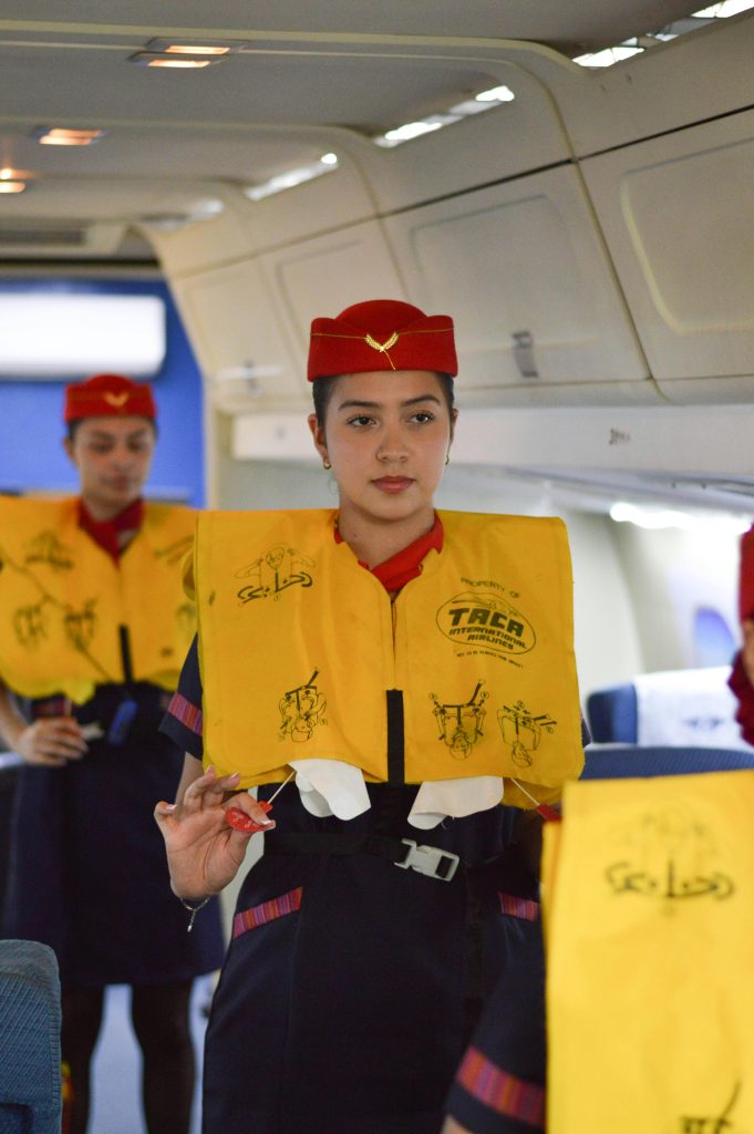 Flight attendants showcasing safety instructions with life jackets on a plane.