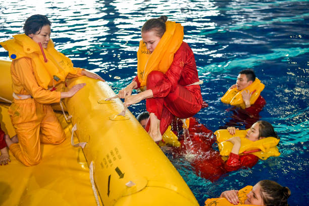 Giovani con indosso giubbotti di salvataggio al centro di una piscina, durante un addestramento. Una donna in tuta rossa sta cercando di salire sul gommone giallo, mentre un’altra donna in tuta gialla è già a bordo