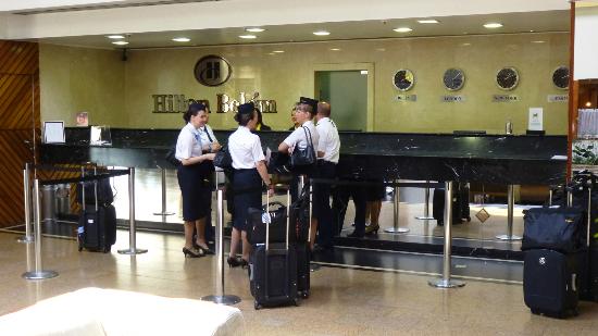 The picture shows a group of cabin crew waiting at the Hilton Hotel reception with their luggage and chatting with each other. 