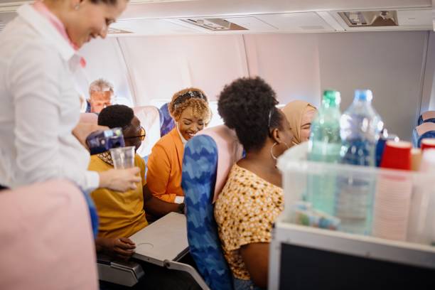 Assistente di volo che sta servendo i passeggeri con delle bevande dal trolley, e i passeggeri sono seduti nei loro sedili di aereo e sorridono