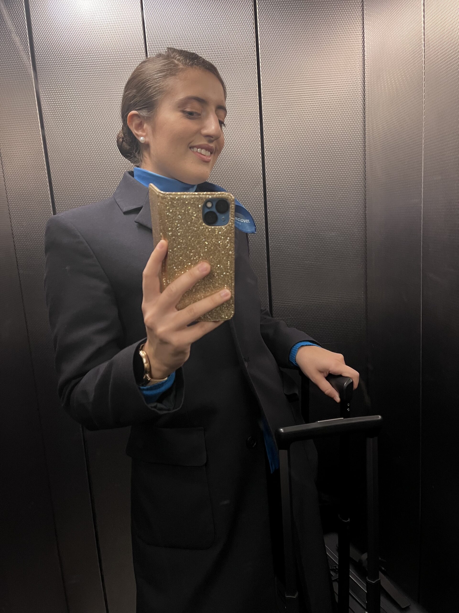 Assistente di volo in uniforme che si fa un selfie con la valigia in mano in un ascensore